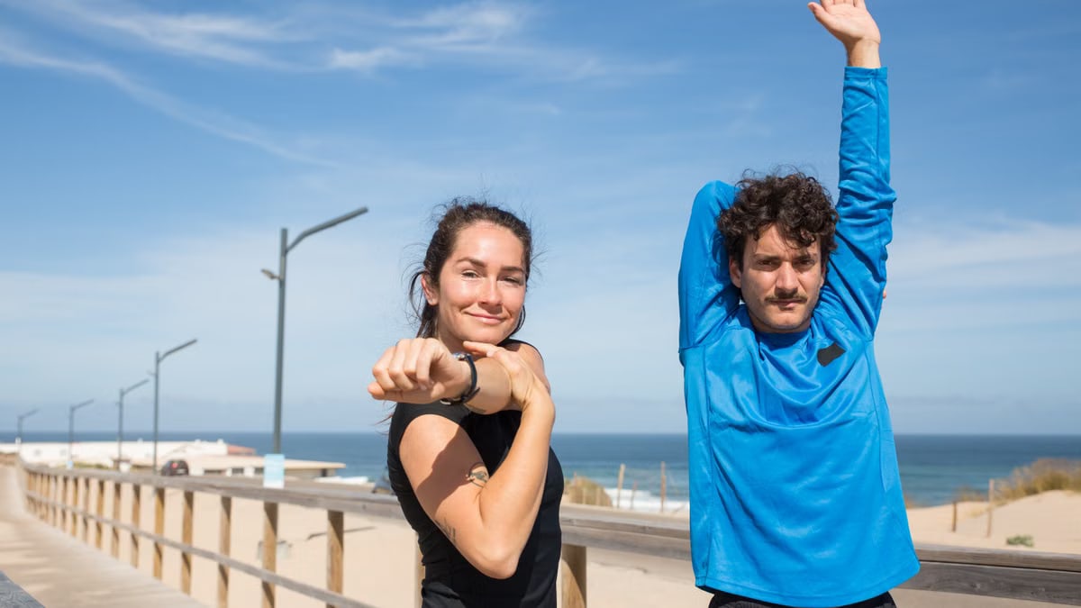 Active young couple stretching outdoors by the ocean on a sunny day in Portugal.
