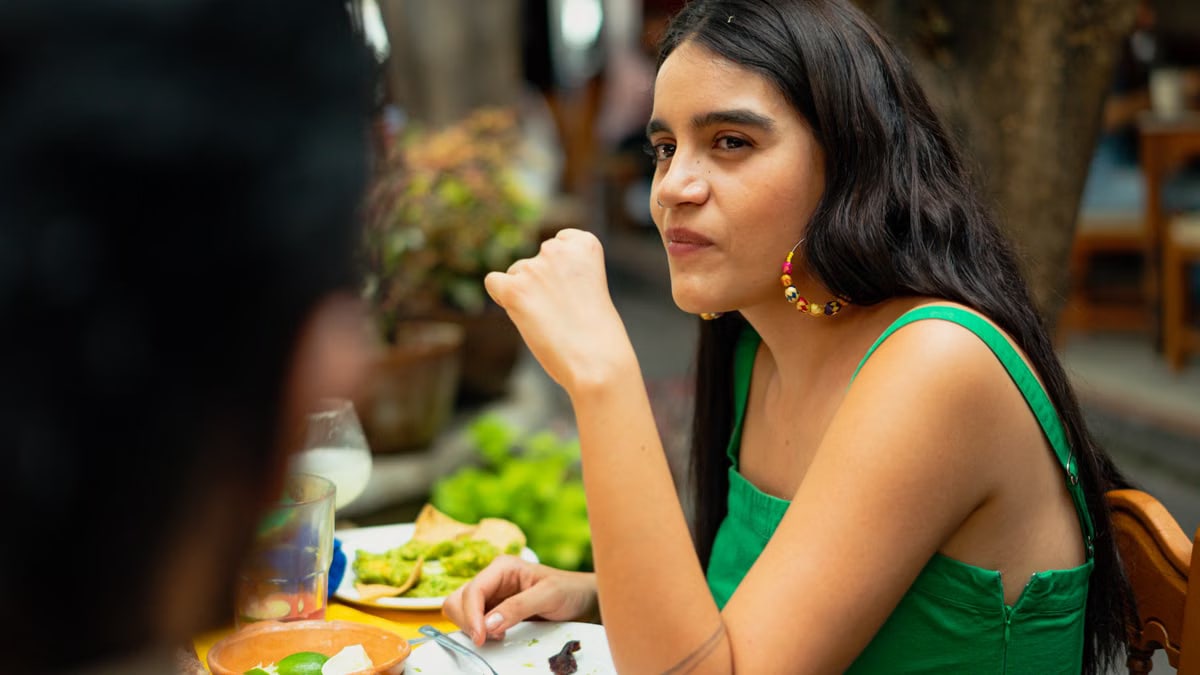 Young woman in green top dining outdoors, enjoying delicious Mexican food on a sunny day.